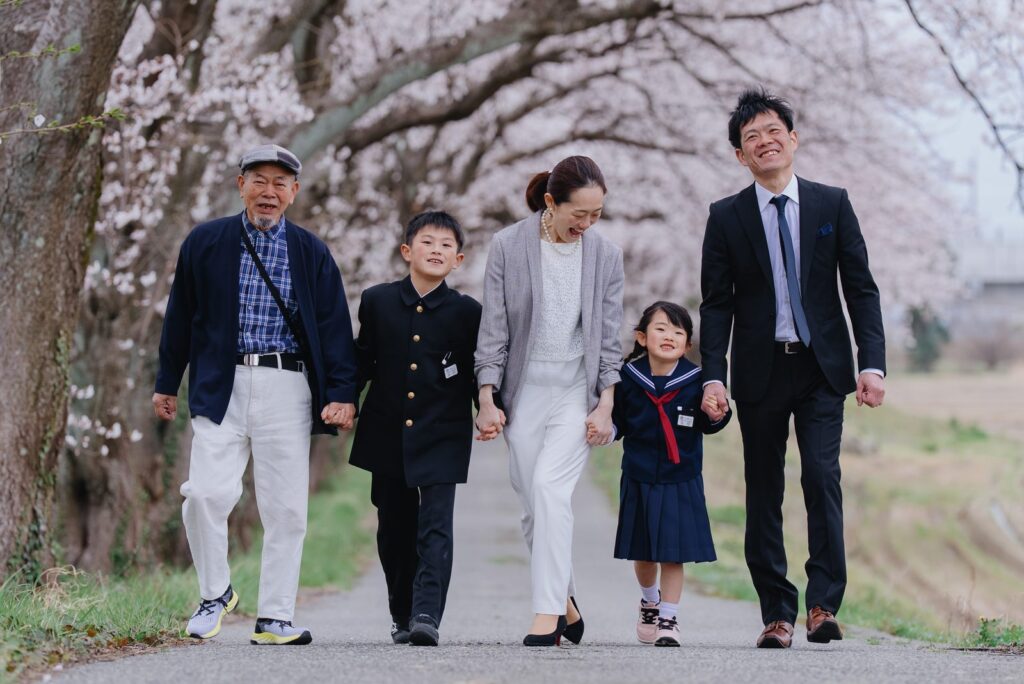 あわら市あらた坂の桜並木を、祖父母と両親、兄妹の三世代6人で歩く家族写真