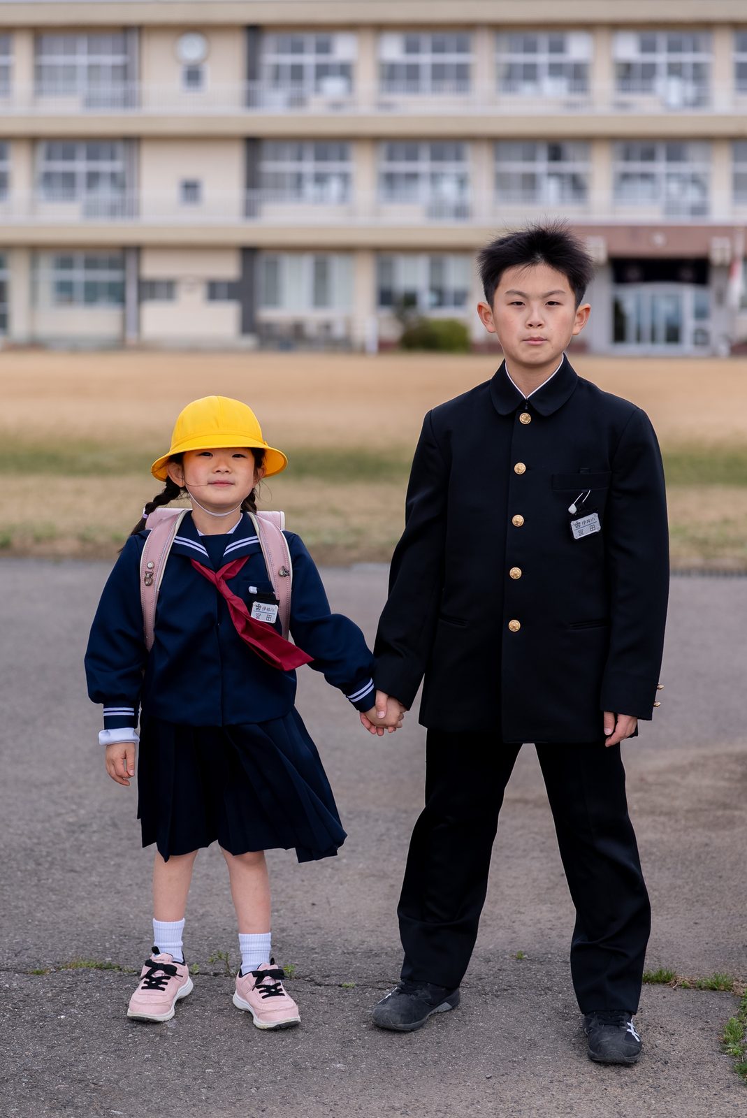 中学の学ラン姿の兄と、黄色い通学帽にランドセルの新一年生の妹が並ぶ