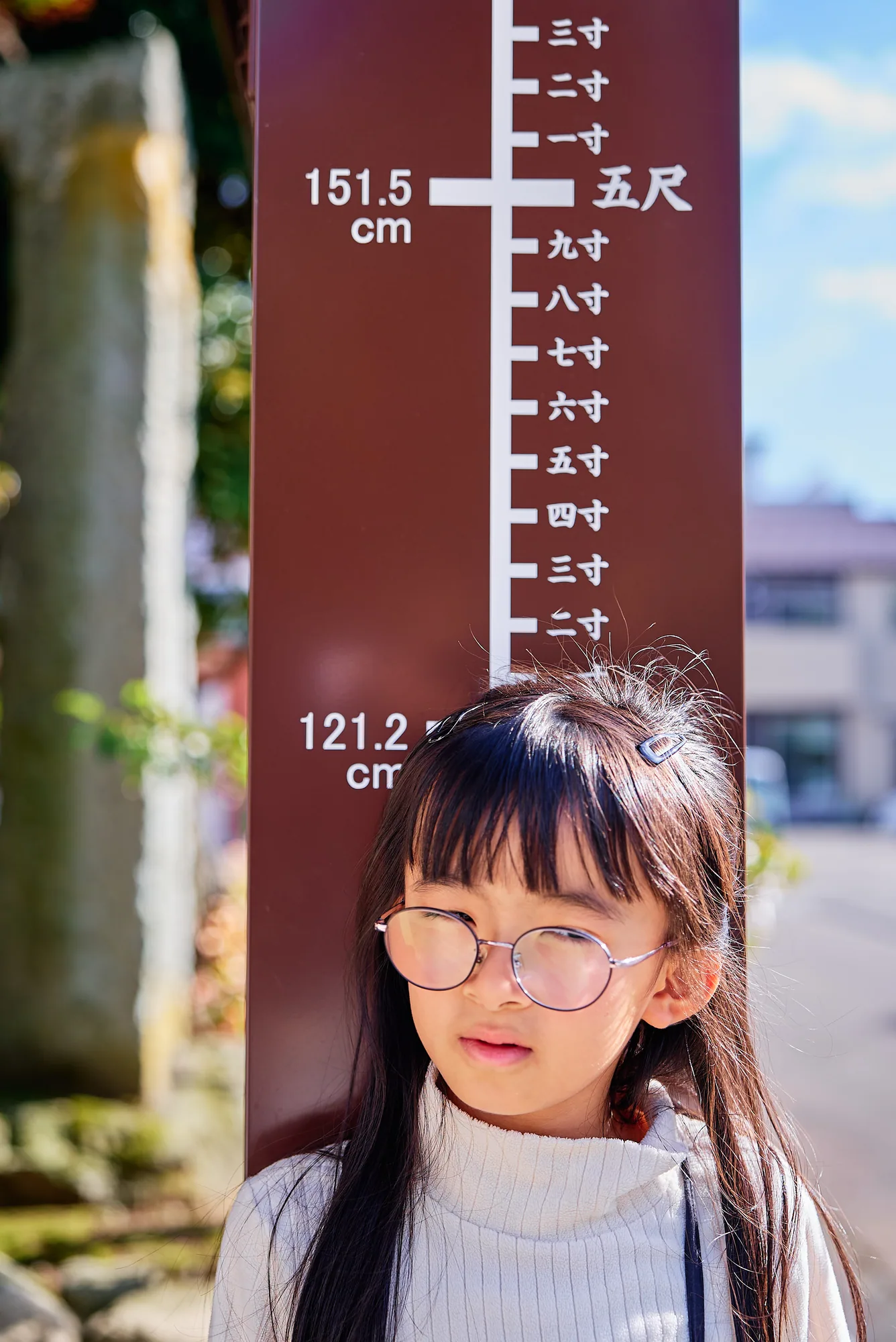 神明神社の身長計の前に立つ7歳の女の子
