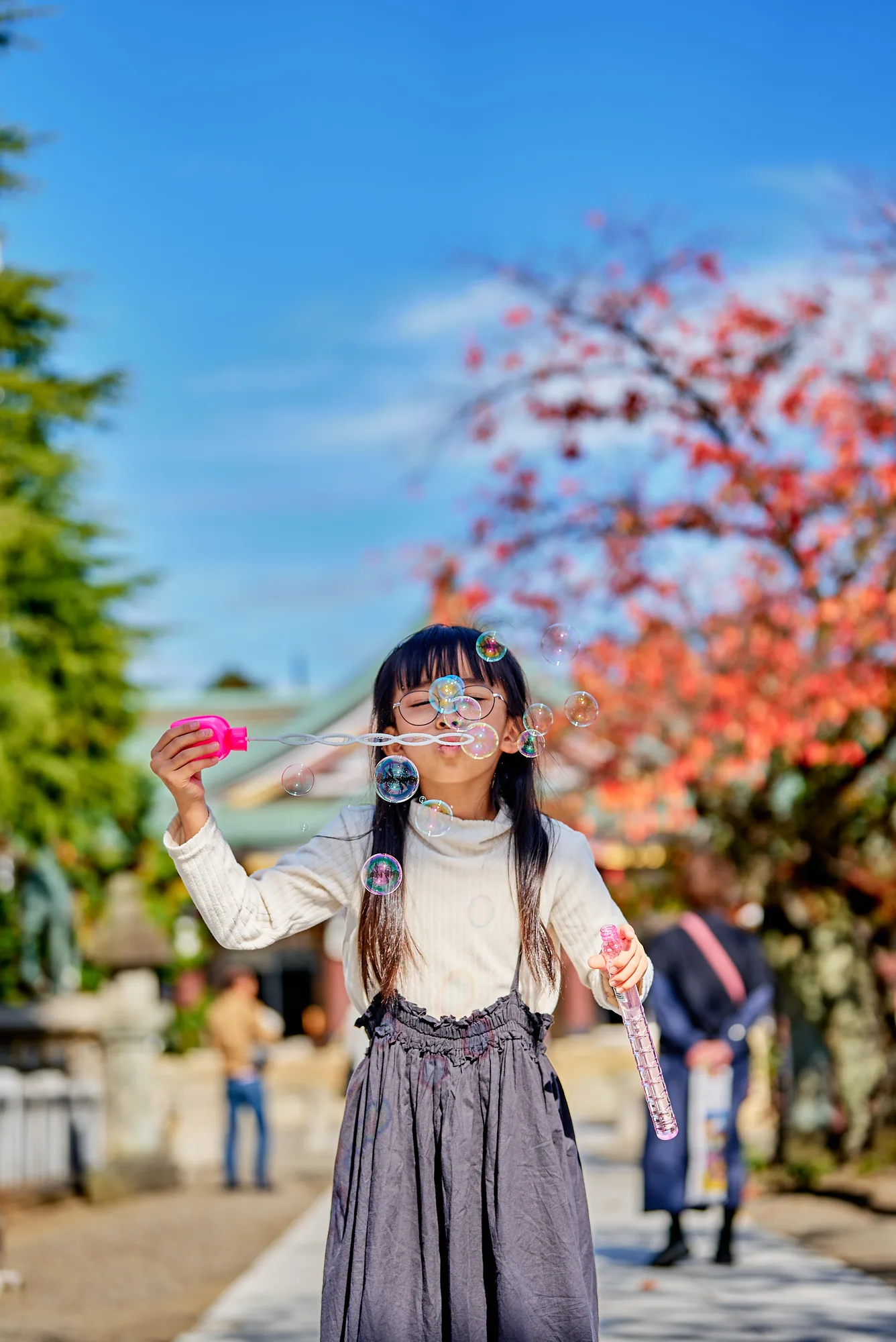 紅葉を背にシャボン玉で遊ぶ7歳の女の子