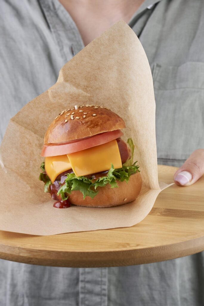 木のボードにのせたハンバーガーを差し出す手